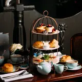 Afternoon Tea in Biggar - Three tier cake stand with Scones, cakes, sandwiches, tea and coffee on a wooden table.